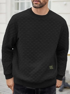 Detail of men's black crewneck sweatshirt with checkerboard jacquard texture and yellow label