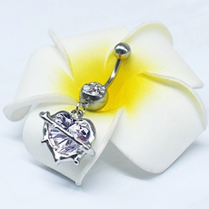 Detailed view of silver heart-shaped navel ring with zircon pendant on a white flower