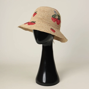 Close-up detail showing intricate red strawberry embroidery on a natural raffia straw hat