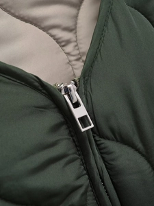 Close-up of metal zipper and diamond quilted texture on dark green jacket neckline