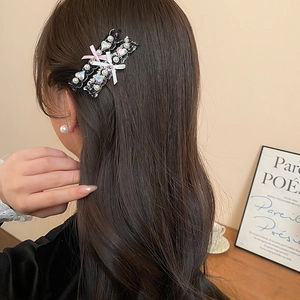 Detail of tweed bow hair clip with pearls and heart gemstone on brown curly hair
