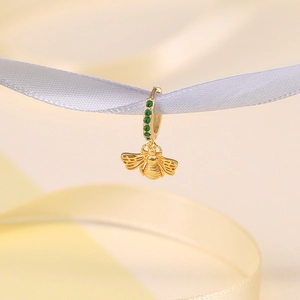 Close-up of golden bee pendant earring with green stones on a white silk ribbon