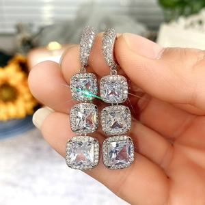 Detailed macro view of triple square-cut halo cubic zirconia drop earrings held by hand