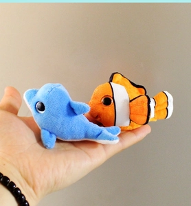 Detailed view of small plush dolphin and clownfish magnets held in hand for size