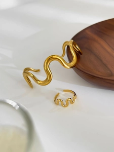 Detailed view of wave-shaped golden bracelet and ring set on minimalist wood display