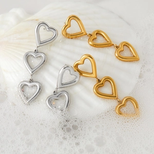 Boucles d'oreilles trois cœurs évidés en or et argent polis sur des coquillages blancs