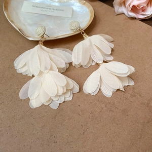 Detail of white raffia chiffon floral tassel earrings with beige woven stud and gold hardware