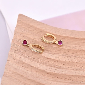 Macro view of gold hoop earrings with small white zircons and a round red stone pendant