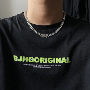 Close-up of a silver Cuban link necklace with Gothic letter pendant on a male model