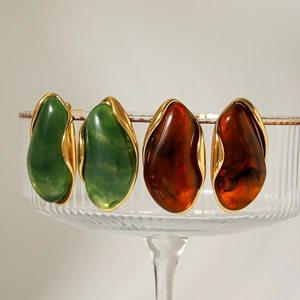 Detailed close-up of resin and gold-plated stainless steel earrings on a glass tray
