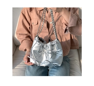 Silver glossy bucket bag with bows and chain strap worn by a model in casual style