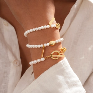 Detailed shot of 18k gold plated pearl bracelets featuring heart charms and OT toggle clasp