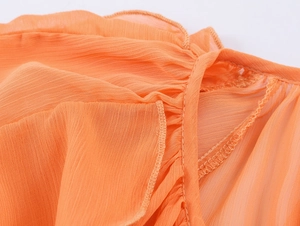 Detail of bright orange ruffled collar and fine stitching on a pleated chiffon shirt