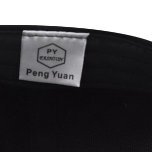 Close-up of the internal PY FASHION brand label stitched on the black cotton baseball cap