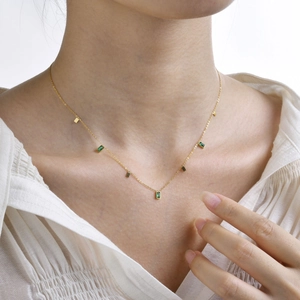 Detail of elegant gold necklace featuring green rectangular zircons on female model