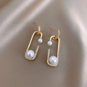 Detailed view of gold safety pin earrings with white pearls and sparkling zircons