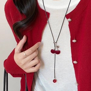 Detail of flocking red cherry and pearl pendant on long black sweater chain necklace