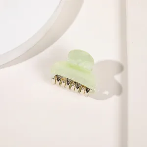Macro detail of a small light green acrylic hair claw clip with metallic teeth on white