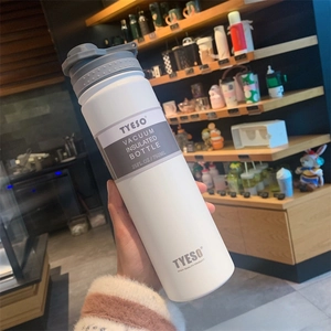 Handheld 750ml white matte insulated water bottle with textured lid in a cafe setting