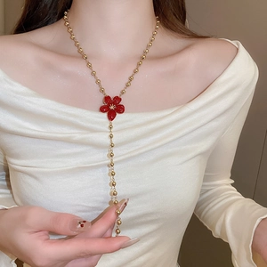 Close-up of a long golden bead Y-necklace with a red flower pendant on a model