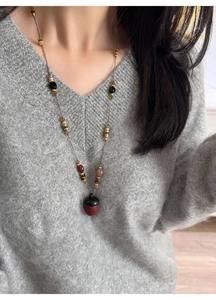 Detail of a vintage-style long necklace featuring an acorn pendant on a grey knitted sweater