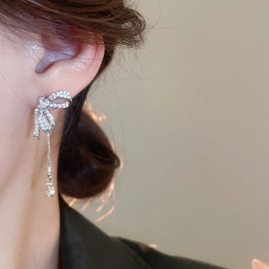 Close-up of a silver bow earring with shimmering zircons and long tassel on an ear