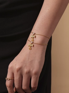 Detail van goudkleurige gelaagde armband met bot- en pootbedeltjes om de pols gedragen