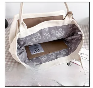 Detail view of the beige canvas tote bag showing the patterned lining and brown leather pocket