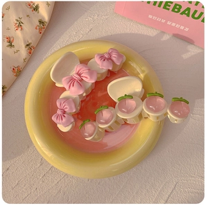 Close-up of a pink peach claw clip and bow hair accessory on a colorful plate