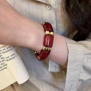 Detail of red acrylic bamboo-joint bracelet with gold beads worn on a wrist