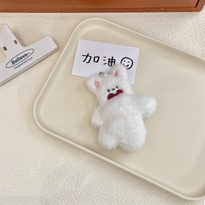 Close-up of fluffy white plush bear keychain with metal clip on a cream tray