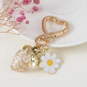 Detail of strawberry charm keychain with golden heart clasp and small daisy ornament