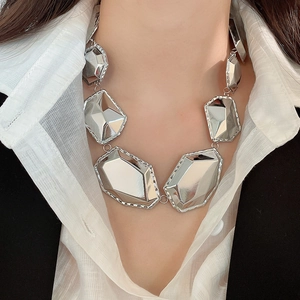 Gros plan d'un collier métallique géométrique argenté aux maillons facettés sur un mannequin