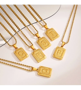 Gros plan de pendentifs initiaux carrés dorés avec des colliers à chaîne torsadée chic
