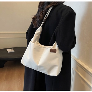 Detail of white nylon tote bag with fashion leather tag shown on a black coat