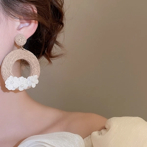 Close-up of bohemian rattan hoop earrings with white fabric flowers and pearl accents