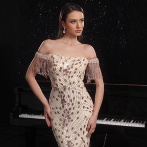 Detalle de vestido de noche beige con lentejuelas y flecos frente a un piano negro mate