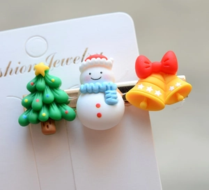 Detail of Christmas hair clips featuring green tree, white snowman, and yellow bell ornaments