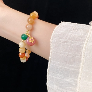 Detail of colorful beaded bracelet with a gold flower pendant on a model wrist