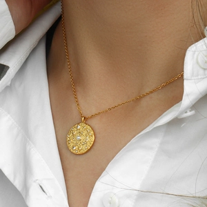 Primo piano della collana a moneta dorata con incisione a stella e zircone su una modella