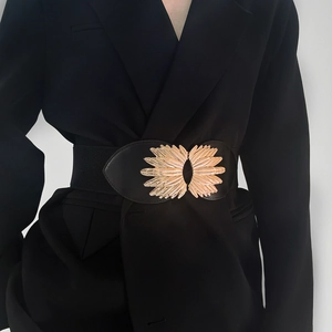 Detail of wide black elastic waist belt with decorative gold wing buckle on a blazer