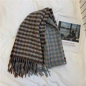 Detail of soft houndstooth scarf with fringe tassels on white bedding for winter warmth