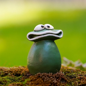 Macro shot of a funny green resin frog statue with big eyes on mossy ground