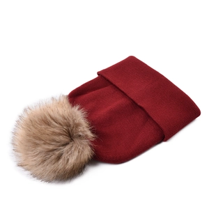 Close-up of wine red knit beanie with a large fluffy light brown faux fur pom pom top