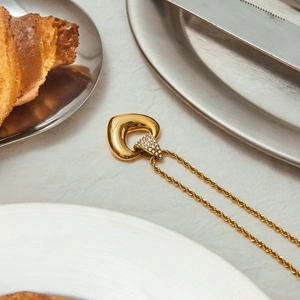 Vue détaillée du collier doré avec triangle en strass sur tissu en lin blanc