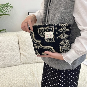 Detail of plush paisley makeup bag with logo tag held in hand for cozy lifestyle vibe
