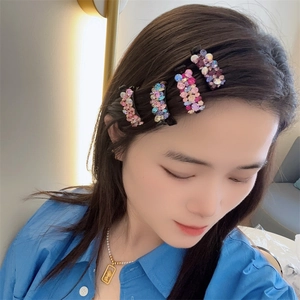 Détail de quatre mini barrettes en strass colorés portées par une femme sous lumière douce