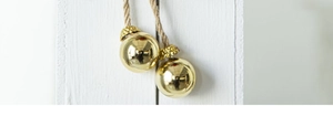 Close-up of golden Christmas ball ornament with woven rope on a white textured wall
