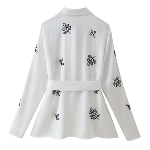Macro detail of black branch embroidery on the back of a white long-sleeved shirt with belt