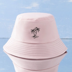 Pink Y2K bucket hat with black palm tree embroidery on light blue wood background